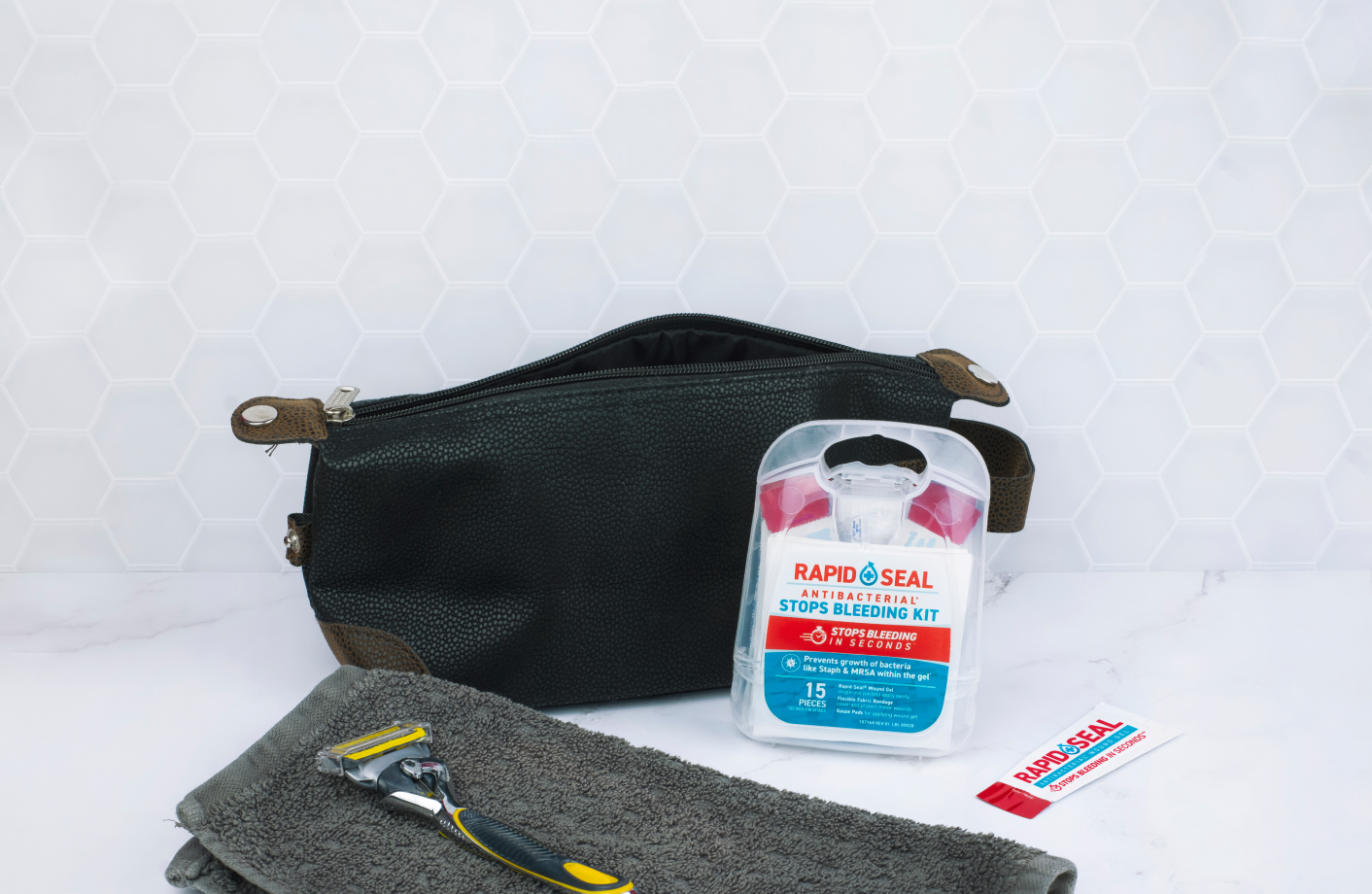 Black toiletry bag with Rapid Seal antiseptic kit, razor, and towel on a white background. image showing the category for kits and packets for rapid seal wound gel