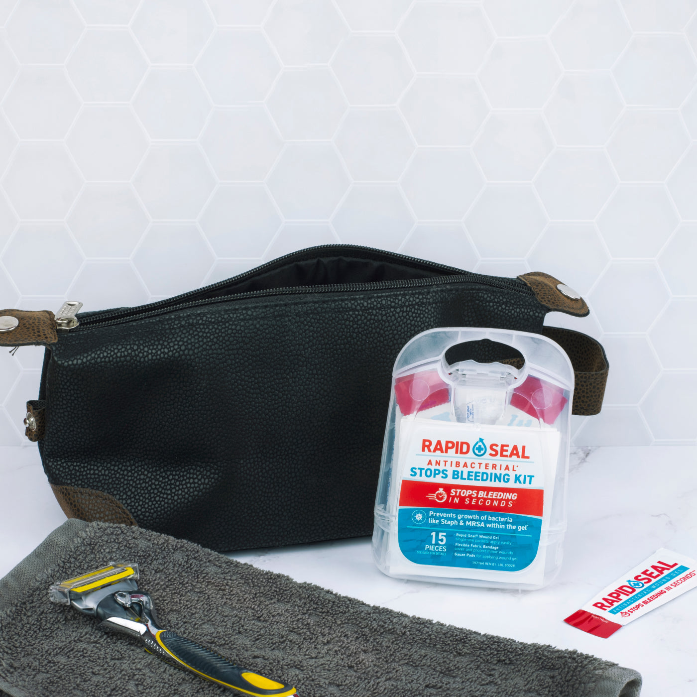 Black toiletry bag with Rapid Seal antiseptic kit, razor, and towel on a white background. image showing the category for kits and packets for rapid seal wound gel